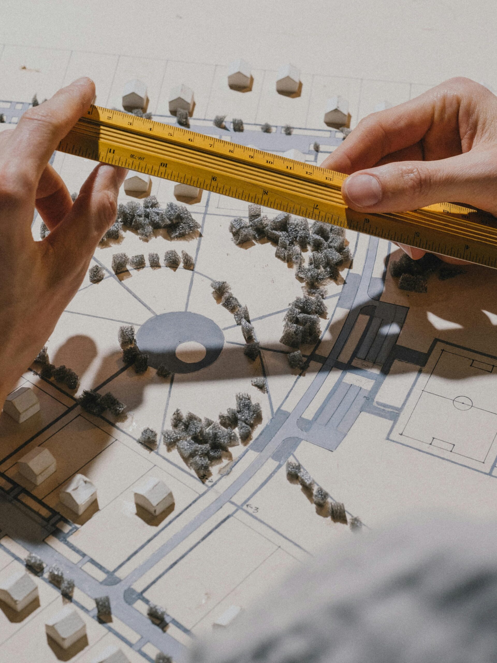 Close-up of hands measuring an architectural model with a ruler under natural light.